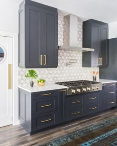 a kitchen with dark blue cabinets and white counter tops, gold trim on the hood