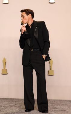 a male in a black suit and glasses holding an award while standing on a carpet