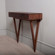 a small wooden table with two drawers on it's sides, against a white wall