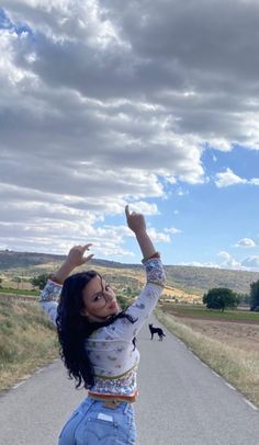 a woman standing on the side of a road with her arms in the air