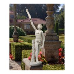 a white statue holding a light pole in front of a garden with flowers and bushes