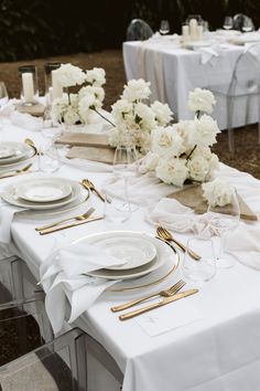 the table is set with white and gold place settings, silverware, and flowers