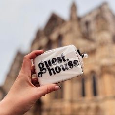 a person holding up a piece of cake with the words guest house on it in front of an old building