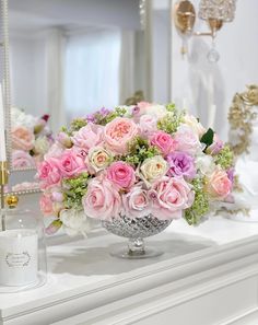 a vase filled with pink and white flowers sitting on top of a table next to a mirror