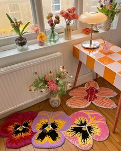 four rugs on the floor in front of a table with vases and flowers