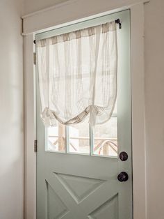 a green door with a white curtain hanging from it's side and a window in the background