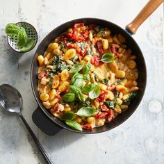 a skillet filled with pasta and spinach on top of a table next to a spoon