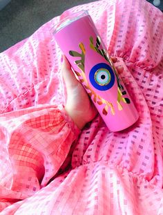 a person holding a pink cup with an evil eye on it and sitting on a bed