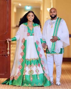 a man and woman dressed in white and green outfits standing next to each other, smiling at the camera