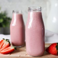 two bottles filled with pink smoothie next to strawberries