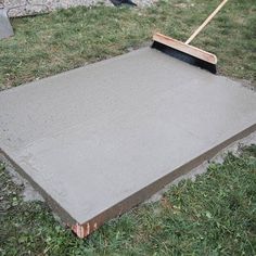 a concrete slab with a broom laying on top of it in the middle of some grass