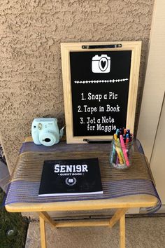 a small table with a sign on it and some pens, pencils, and a camera