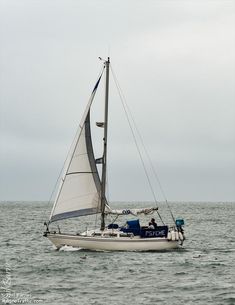 a sailboat sailing in the ocean on a cloudy day with no one around it