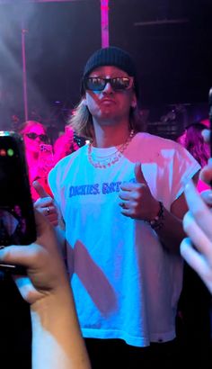 a man with sunglasses and a hat on taking a selfie in front of a group of people