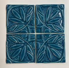 four blue tiles with leaves on them are arranged in the shape of square tiles,