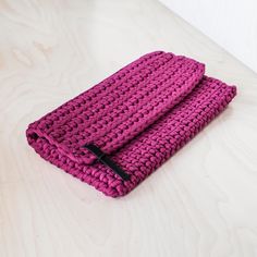 a pink knitted towel sitting on top of a wooden table next to a black object