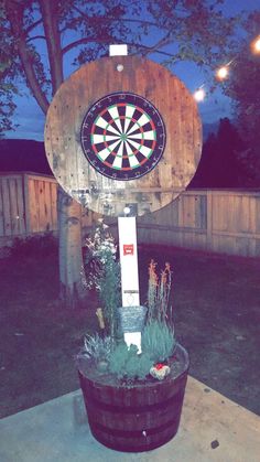 a dart board mounted to the side of a wooden barrel with plants in front of it