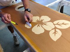 a man is painting a flower on a wooden table with white paint and yellow marker