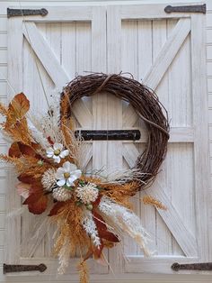 a wreath with dried flowers and leaves is hanging on a barn door, ready to be hung