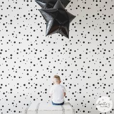 a young boy sitting on top of a suitcase under a black star wallpapered room