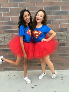 two girls dressed up as superman and wonder in front of a brick wall with their arms around each other