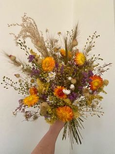 a hand holding a bouquet of wildflowers and grasses