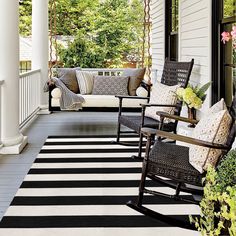 a porch with black and white striped rugs on the floor, rocking chairs and potted plants