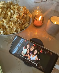 a cell phone sitting on top of a table next to a bowl of popcorn and candles