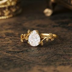 a gold ring with a pear shaped diamond in the center on a wooden surface next to other jewelry items