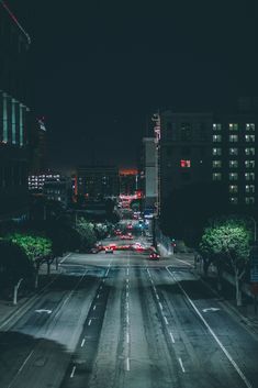 an empty city street at night with cars driving on it and buildings in the background