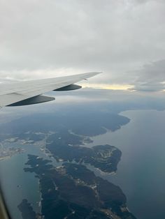 the wing of an airplane as it flies over water and land in front of a cloudy sky