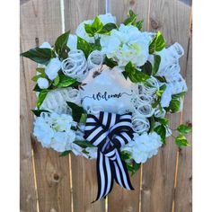 a wreath with white flowers and black ribbon hanging on a wooden fence that says welcome