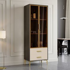 a tall cabinet with glass doors and gold trimmings in a living room next to a lamp