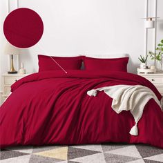 a bed with red sheets and pillows in a room next to a white dresser, potted plant and lamp