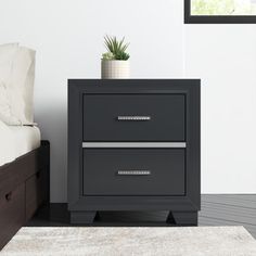 a nightstand with two drawers and a plant on top of it next to a bed