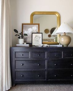 a dresser with a mirror, lamp and pictures on it