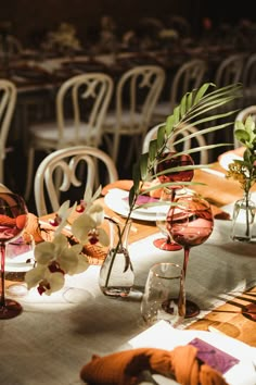 the table is set with glasses, plates and flowers in vases on top of it