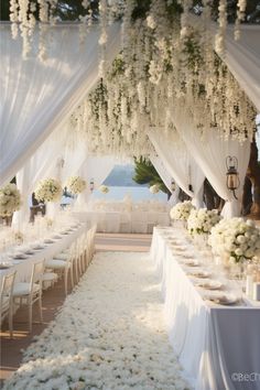 an outdoor wedding setup with white flowers and greenery on the ceiling, along with long tables