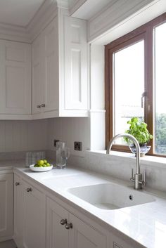 a kitchen with white cabinets and marble counter tops, along with a bowl of fruit on the window sill