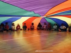 several children sitting on the floor in front of large colorful umbrellas