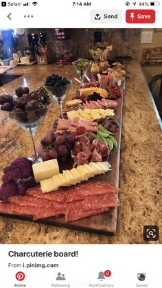 an assortment of cheeses, meats and grapes on a wooden platter with wine glasses