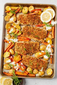 baked fish with lemons, potatoes and carrots on a baking sheet in a pan