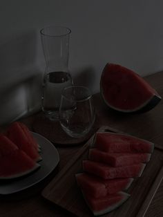 slices of watermelon sit on plates next to a glass and pitcher, along with another piece of watermelon