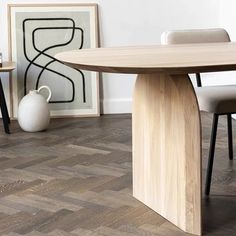 a wooden table and chairs in a room with white walls, wood flooring and artwork on the wall