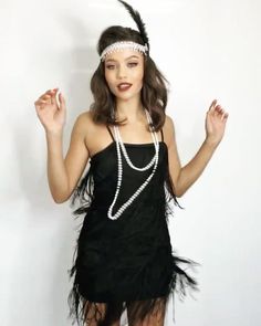 a woman in a black flap dress with pearls and feathers on her head is posing for the camera