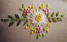 a white flower with yellow and pink flowers is on the back of a tan pillow