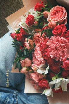 a bouquet of pink and red flowers sitting on someone's lap