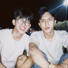 two young men sitting next to each other in front of a street light at night