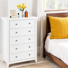 a white dresser sitting next to a bed with yellow pillows and flowers on top of it