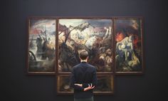 a man standing in front of two paintings with his back to the camera, looking at them